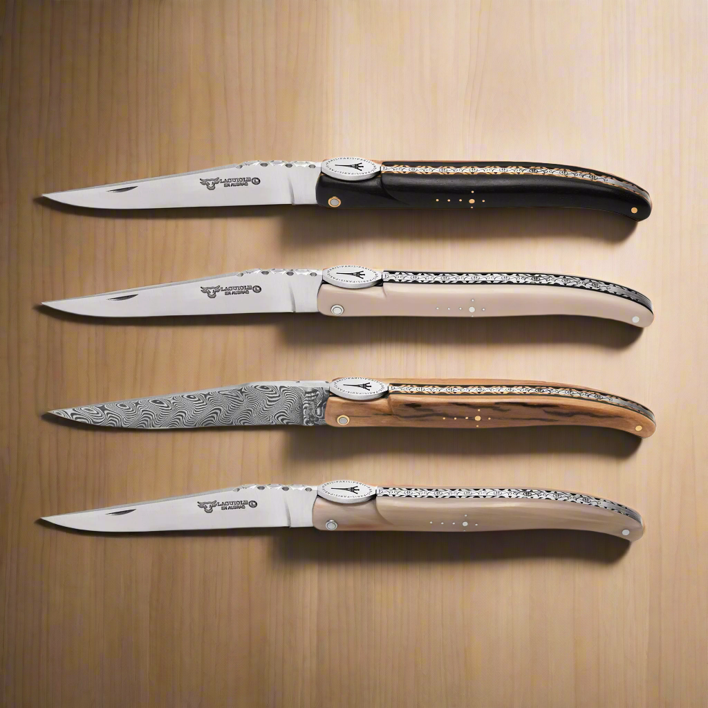 Four Laguiole en Aubrac Eiffel Collection folding knives with different blade designs on a wooden surface