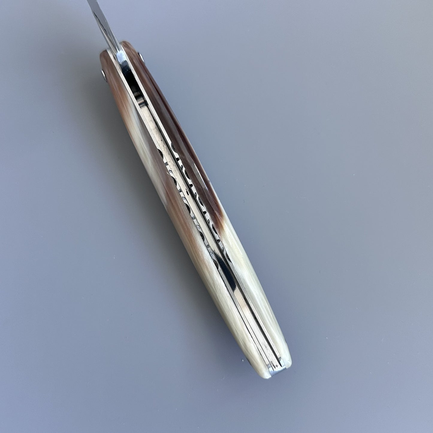 A folding pocket knife with a polished horn handle showing natural brown and cream marbling, and a silver metal blade partially extended, set against a solid gray background.
