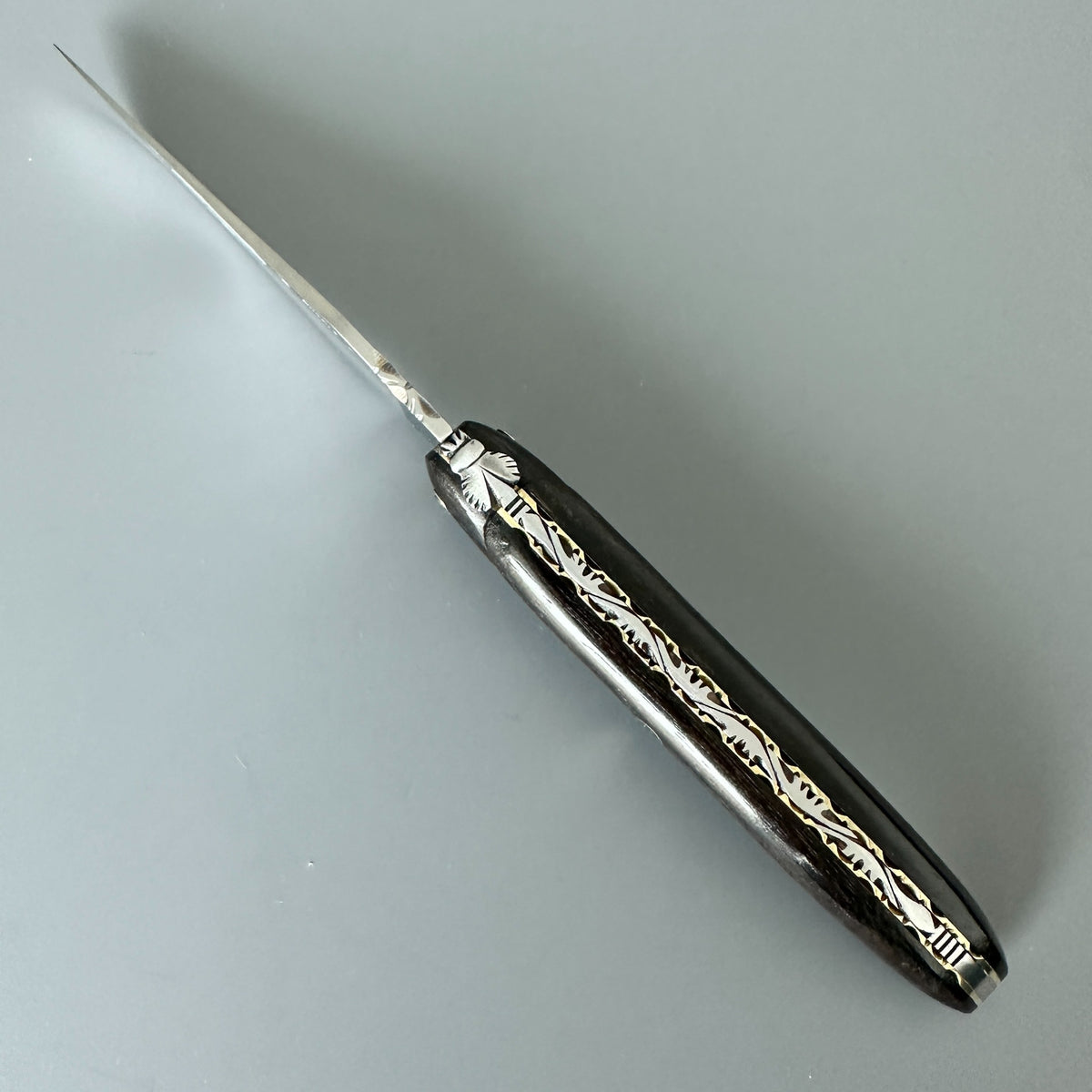 Cenital view of Laguiole en Aubrac folding knife with Ebony handle, stainless and brass spine.