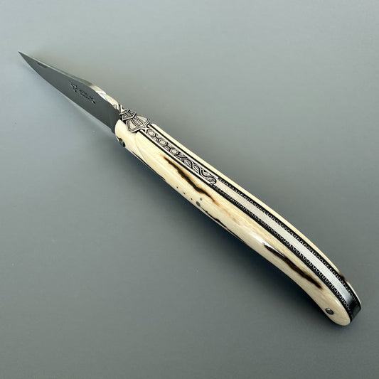 Open Laguiole en Aubrac mammoth ivory folding knife with dark handle streaks on a gray background.