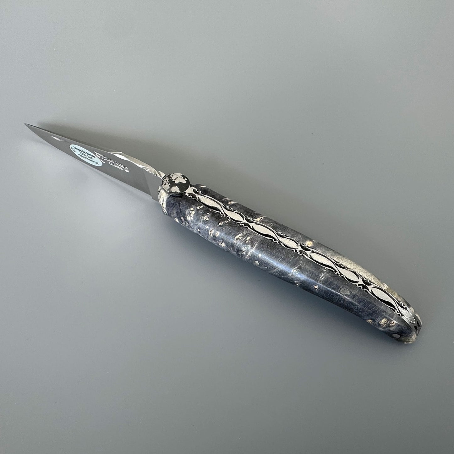 Laguiole enAubrac pocket knife with a marbled mightnight burl and silver blade, shown on a neutral gray background.