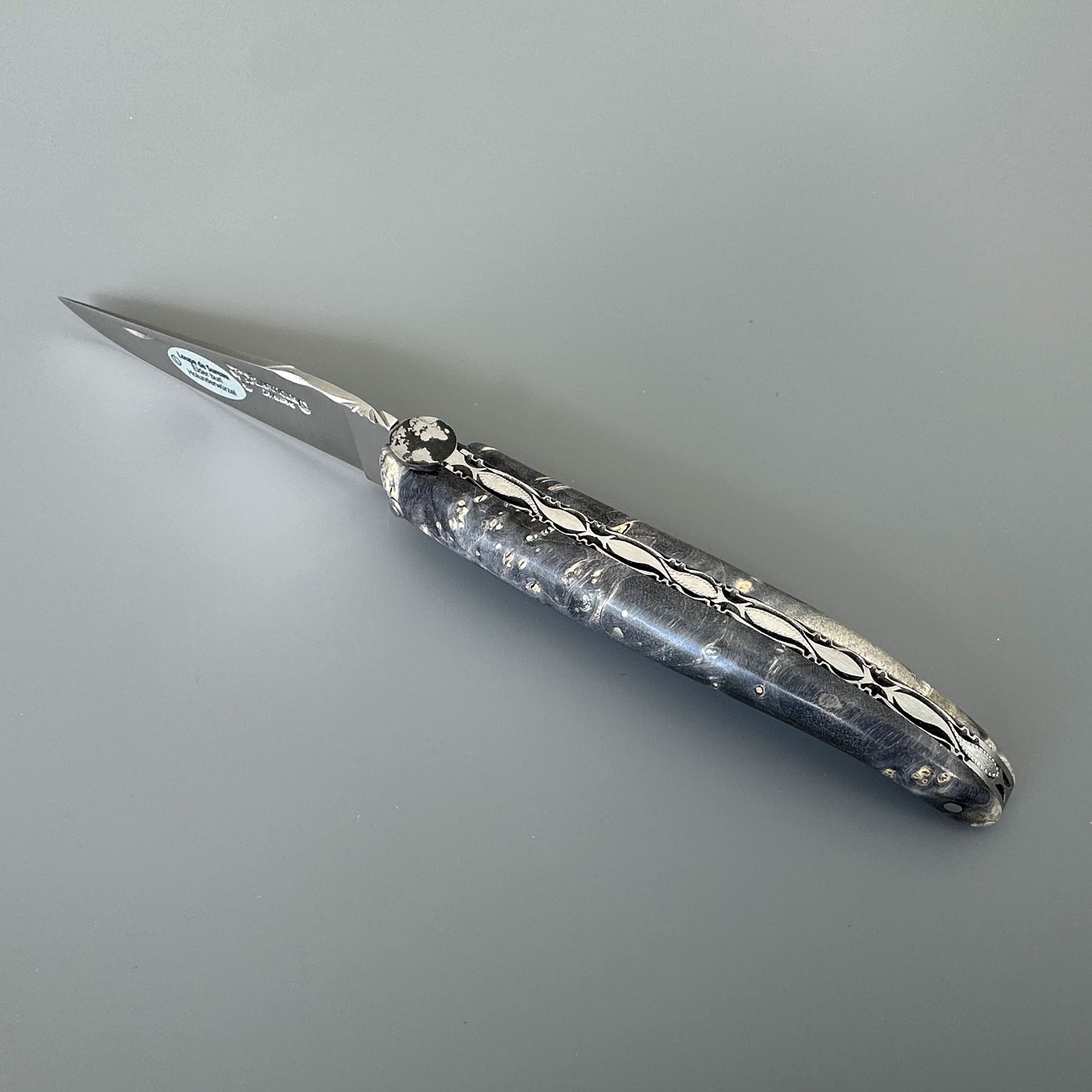 Laguiole enAubrac pocket knife with a marbled mightnight burl and silver blade, shown on a neutral gray background.