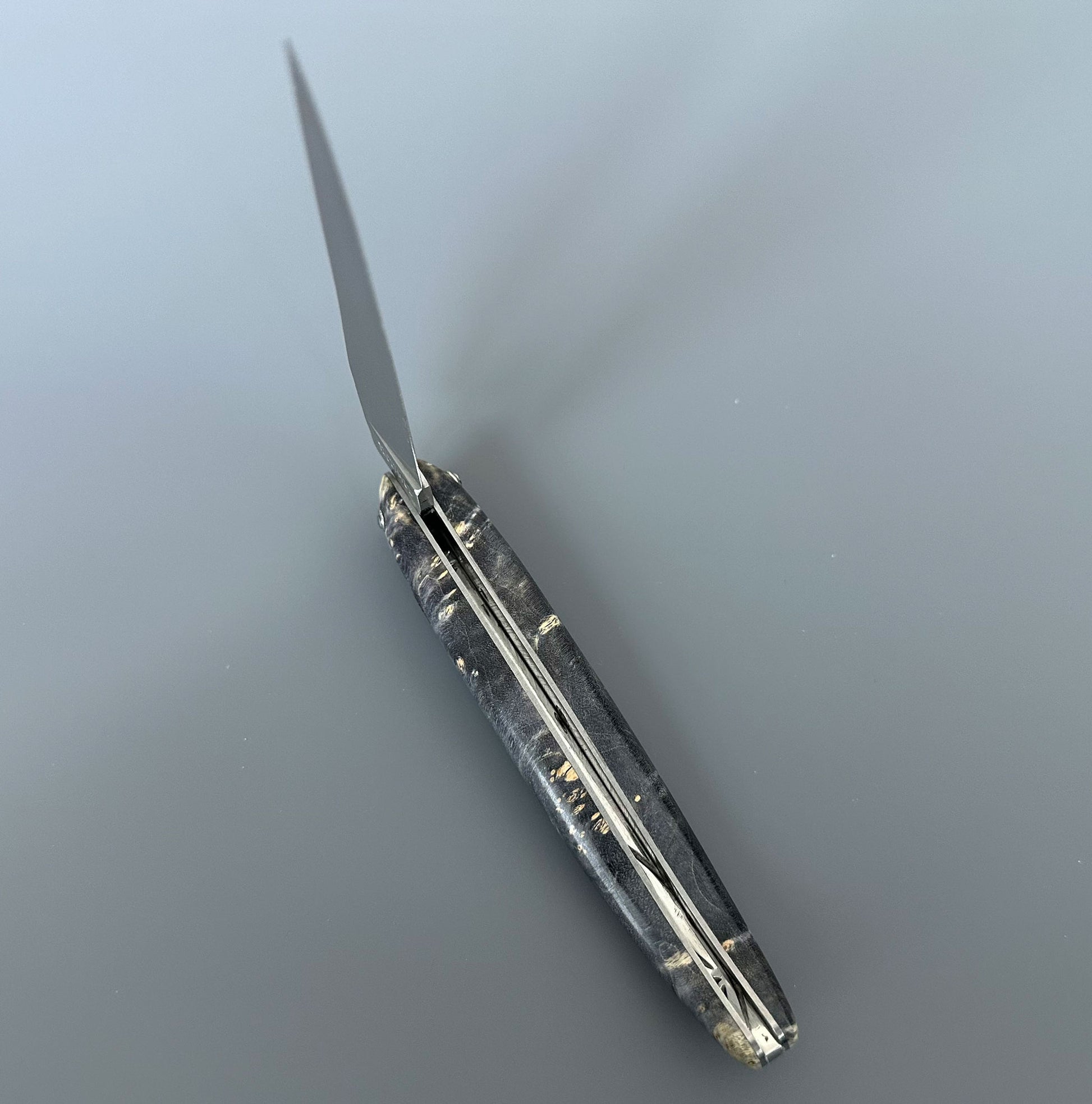 A folding pocket knife with a black burl handle, shown partially open on a smooth gray surface.