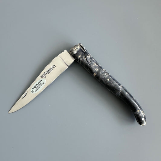 Laguiole en Aubrac folding pocket knife shown open on a solid gray background. The blade is engraved and handle is made of might Earl Burl