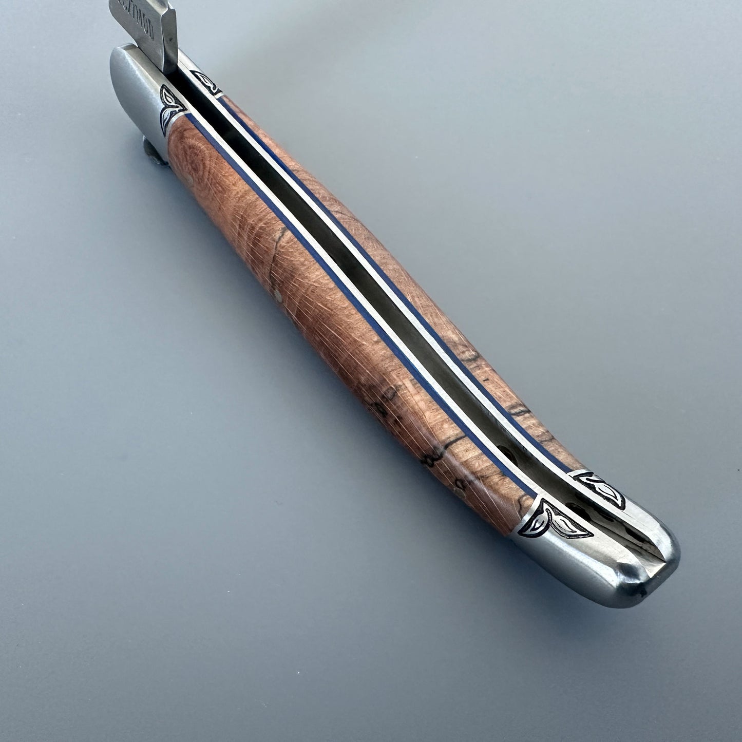 Inner Spine view of a Laguiole en Aubrac Belle Piece folding knife with wood handle, blue spacer and engraved bolsters