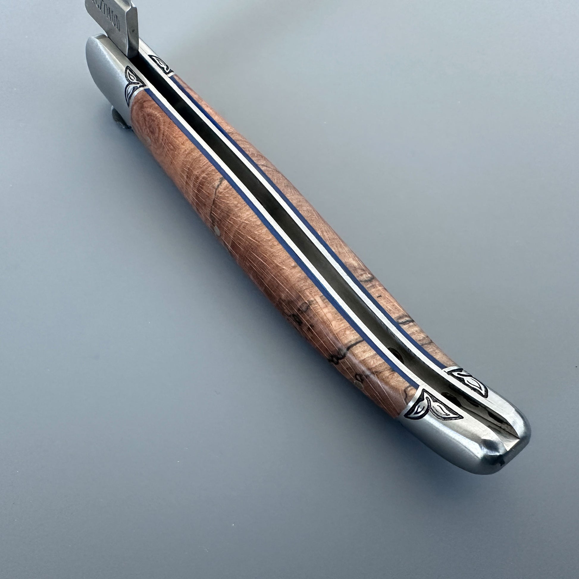 Inner Spine view of a Laguiole en Aubrac Belle Piece folding knife with wood handle, blue spacer and engraved bolsters