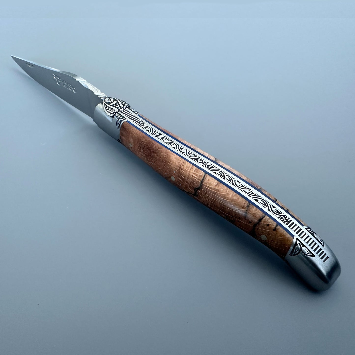 Spine view of an open Laguiole en Aubrac Belle Piece knife with wood handle, blue spacer and decorated bolsters