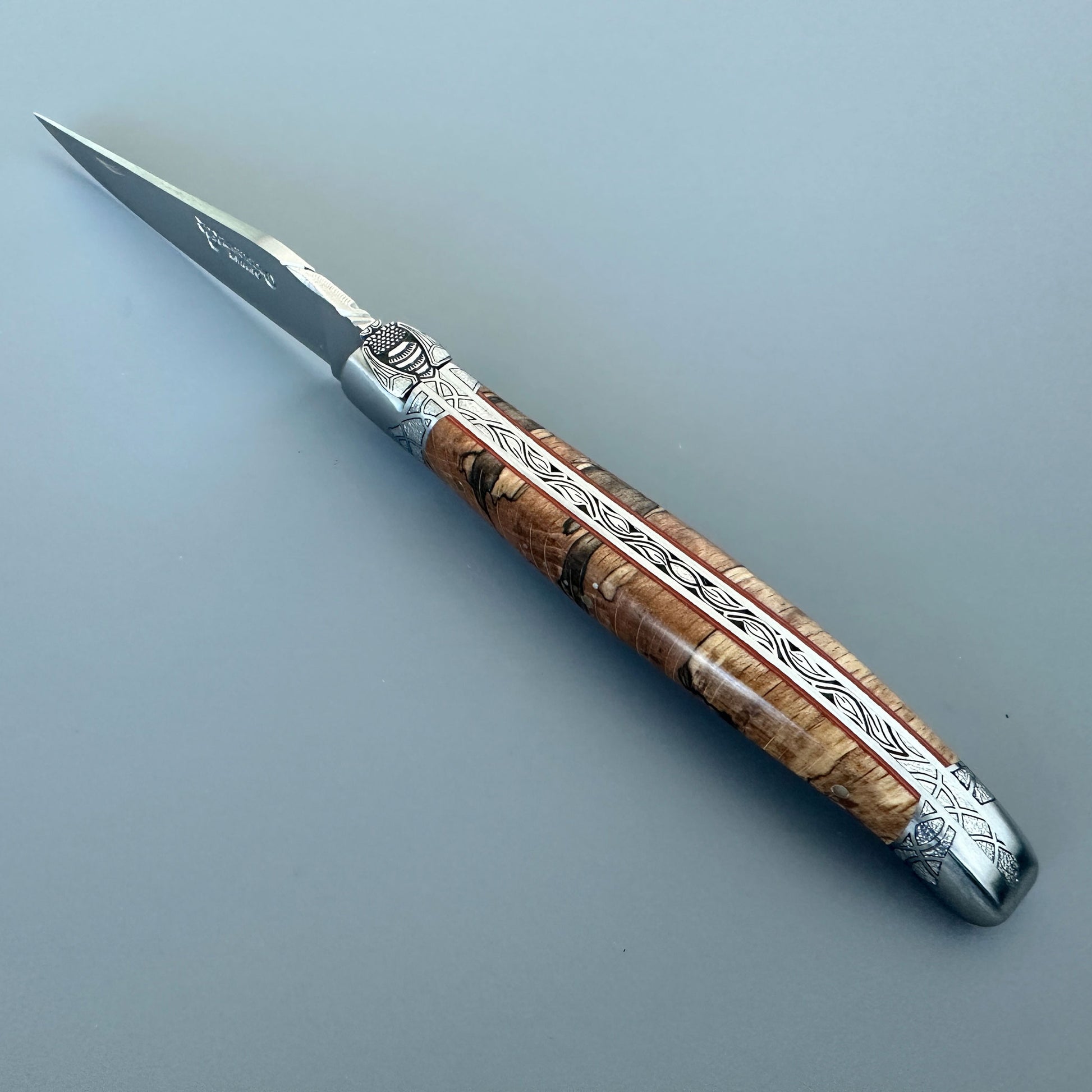 Open front view of a Laguiole en Aubrac Belle Piece folding knife with wood handle, red spacer and engraved bolsters