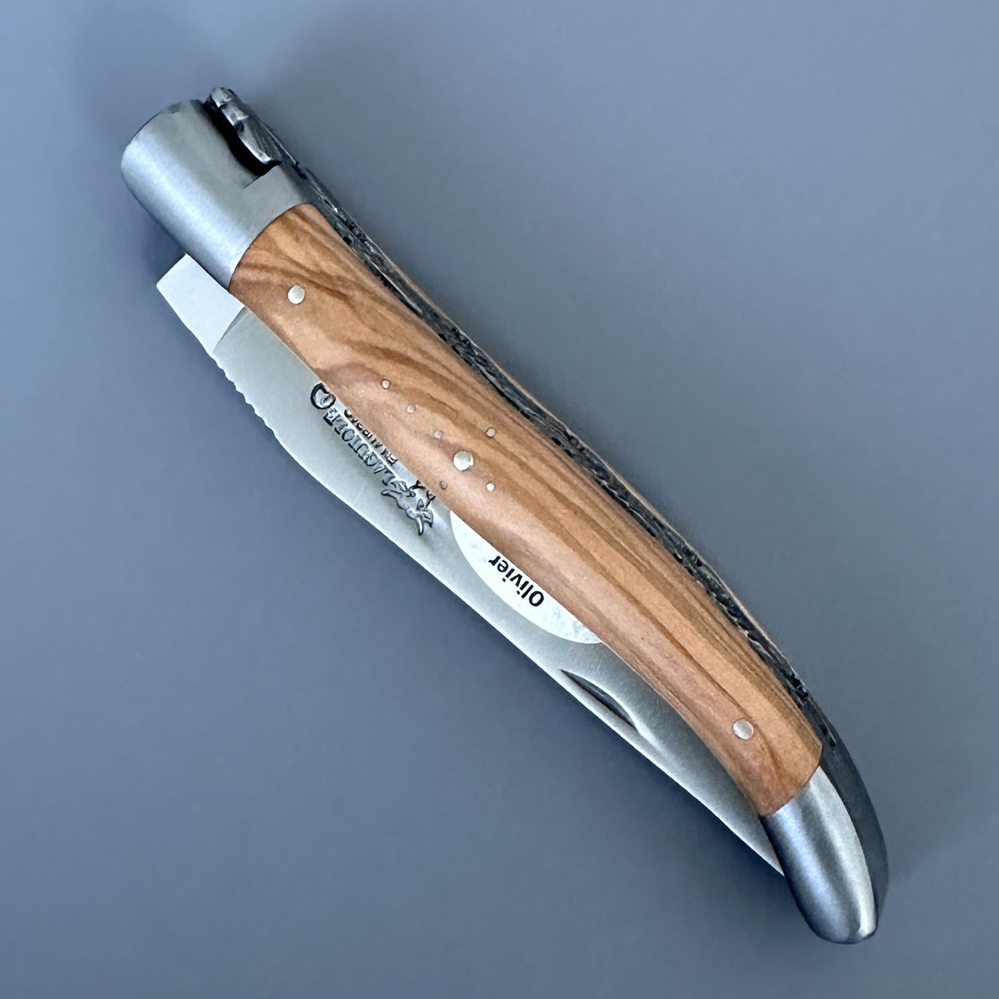 Top-down view of the closed Laguiole Double Plated knife showing the olive wood handle with fishtail engraved bolster and nickel silver liners.