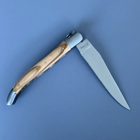 Reverse side of the Laguiole Double Plated knife, closed, showing the olive wood handle, brass pins, and "Olivier" label on the blade.