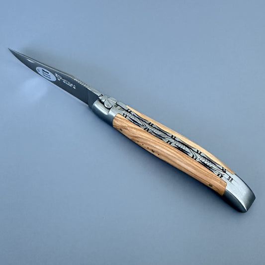 Laguiole Double Plated folding knife fully open, showing the polished blade, engraved bee bolster, and olive wood handle with decorative filework.