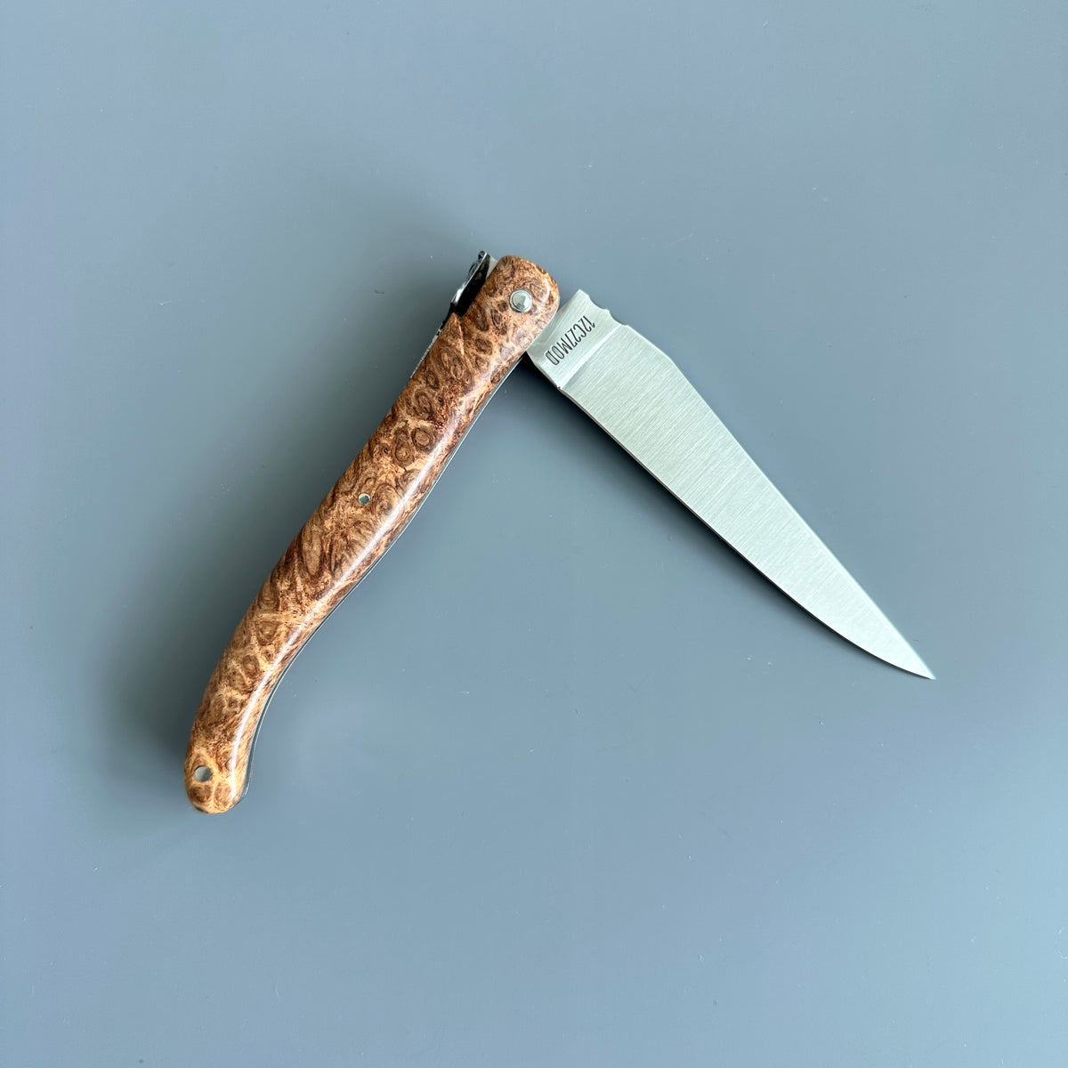 Reverse side of Laguiole en Aubrac folding knife with Amboyna burl wood handle partially open.
