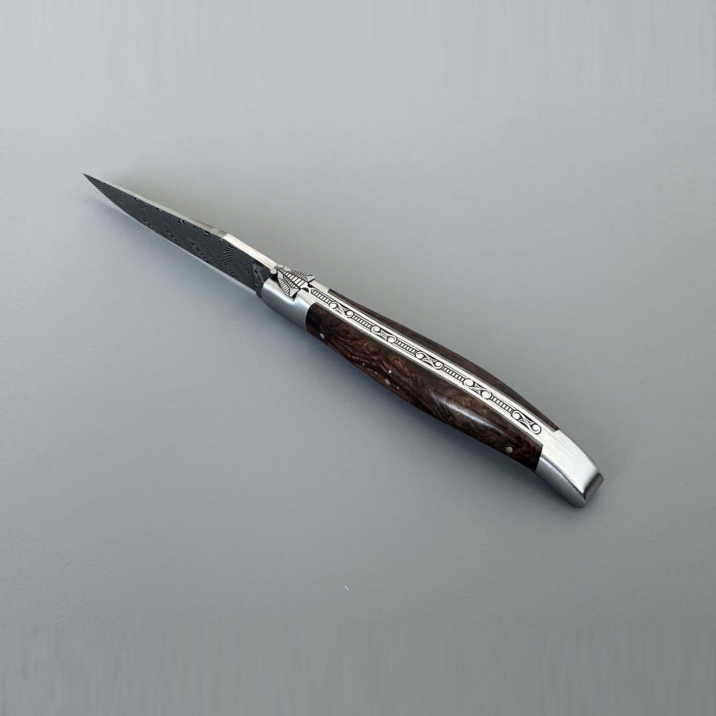 Fully open Laguiole en Aubrac Belle Double Plated knife showing the Damascus blade, nickel silver bolster with engraved Bee motif, and Ironwood handle scale.