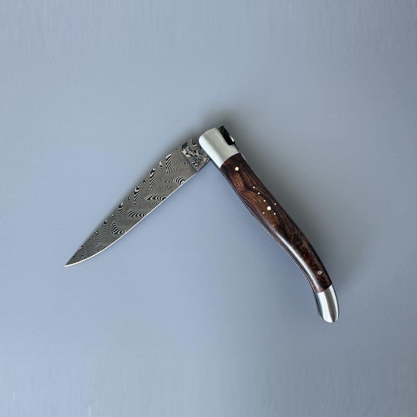 Laguiole en Aubrac Belle Double Plated folding knife with Damascus steel blade partially open, showing the wavy Damascus pattern and dark Ironwood handle