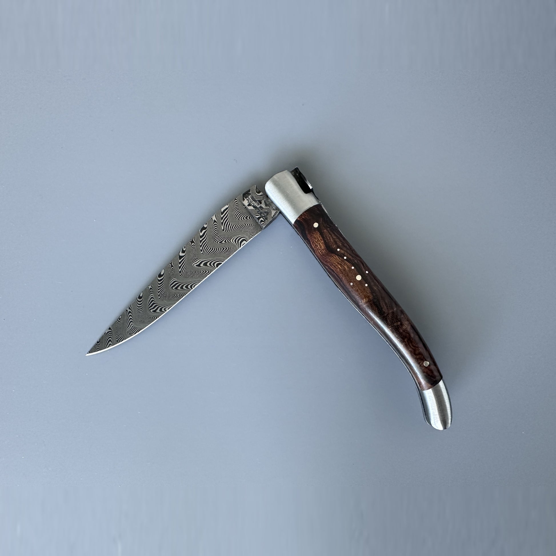 Laguiole en Aubrac Belle Double Plated folding knife with Damascus steel blade partially open, showing the wavy Damascus pattern and dark Ironwood handle