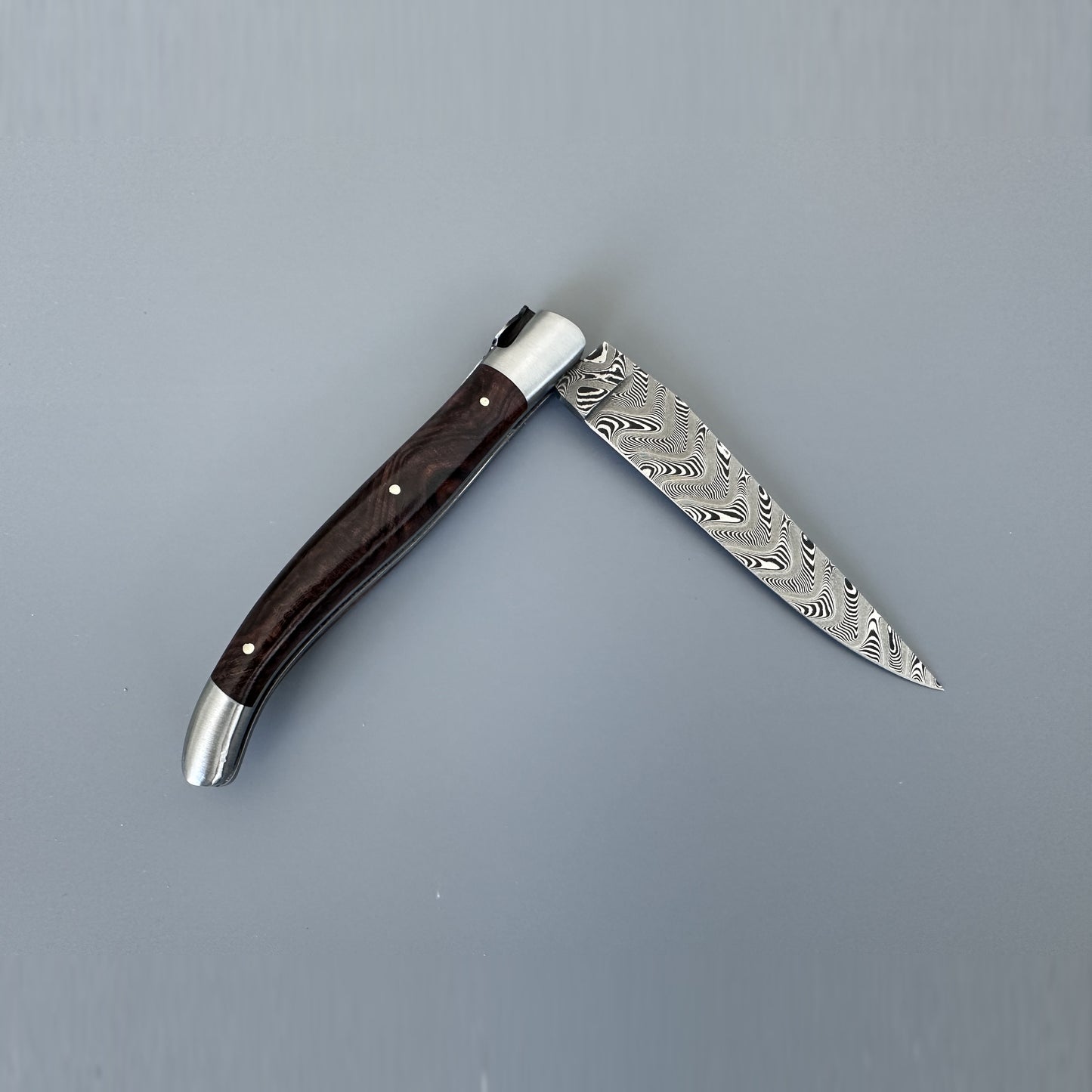 A folding pocket knife with a Damascus steel blade and a dark brown wooden handle, shown open against a solid gray background.