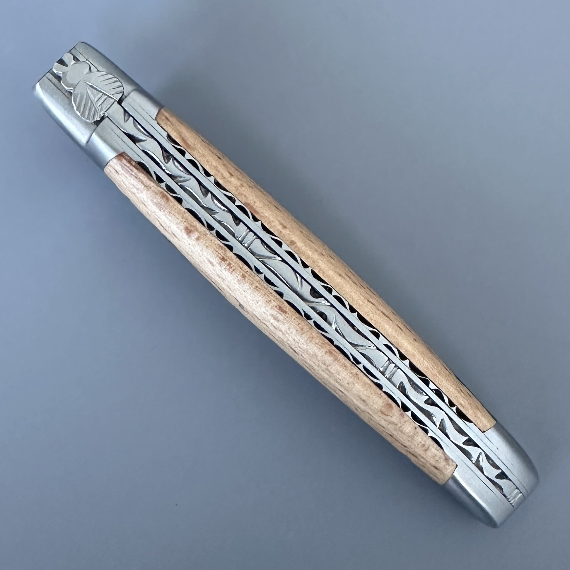 Closed Laguiole Double Plate Damascus knife showing the engraved bee bolster and pierced filework along the spine.
