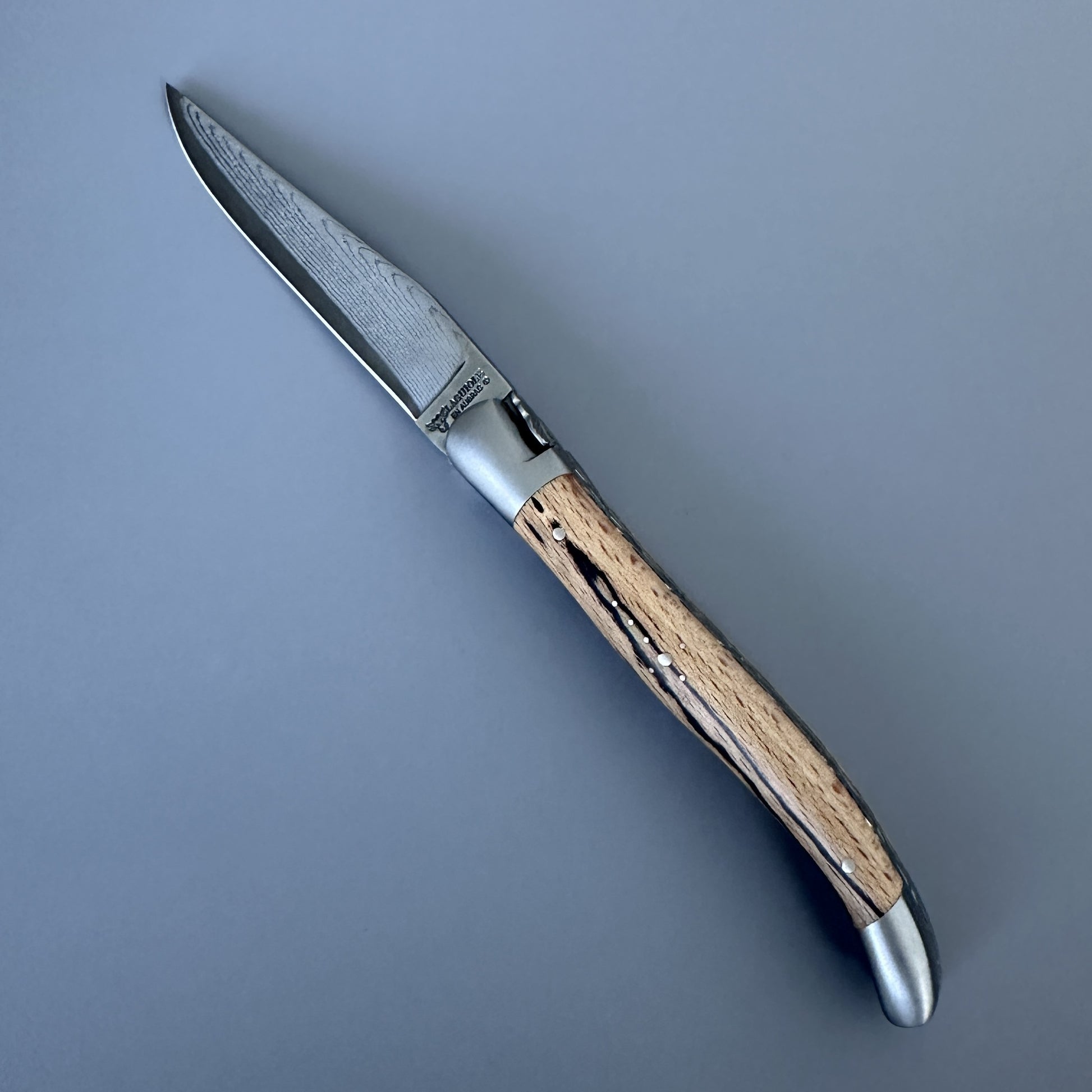 Laguiole Double Plate Damascus knife open, angled to show the engraved leaf bolster and Damascus blade pattern.