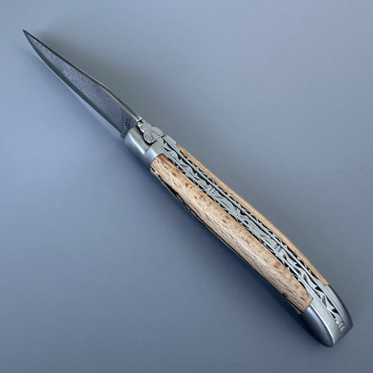 Laguiole Double Plate Damascus folding knife with Aubrac wood handle, blade open, on a blue background.