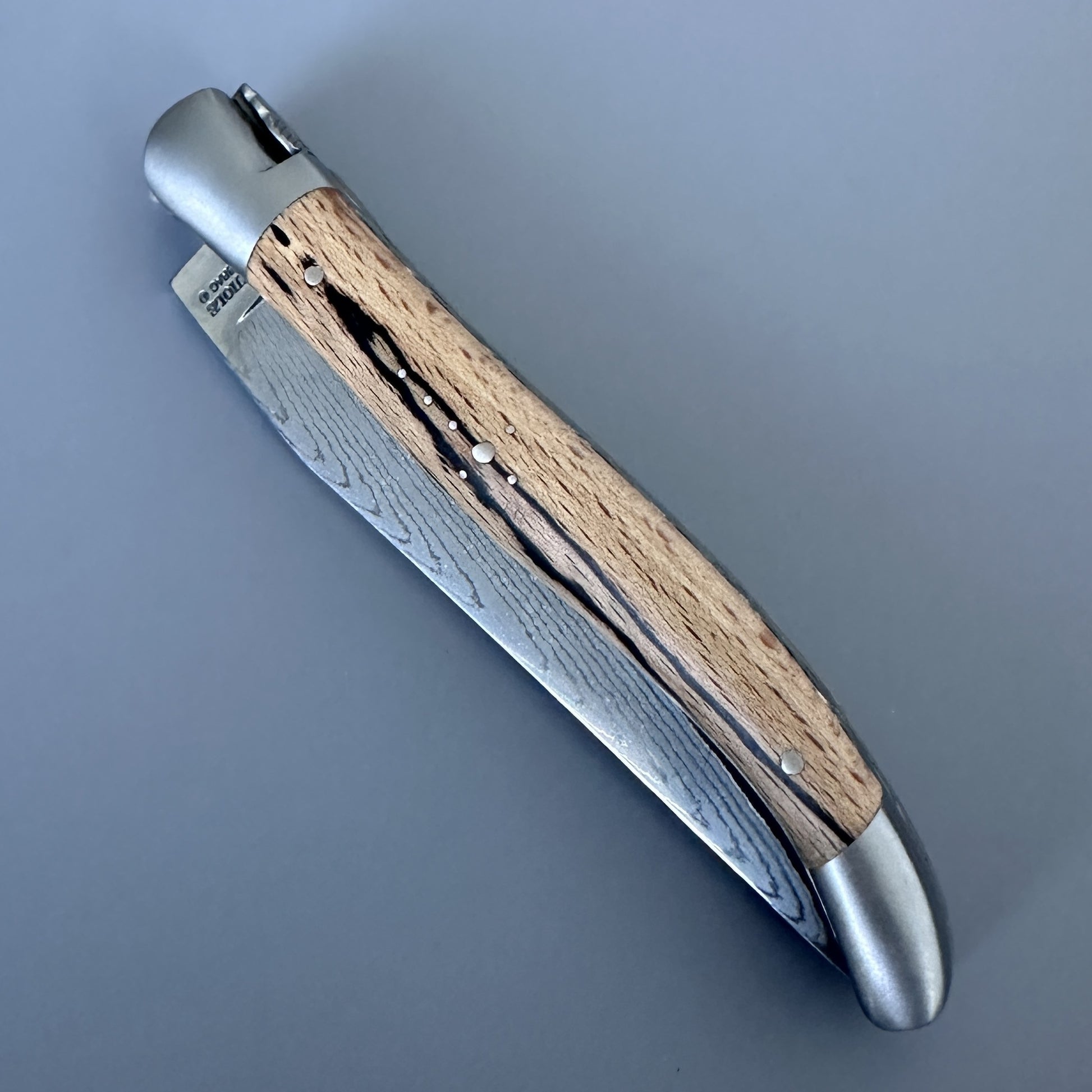 Top-down view of the closed Laguiole Double Plate Damascus knife, showing the pierced filework bolster and Aubrac wood scales.