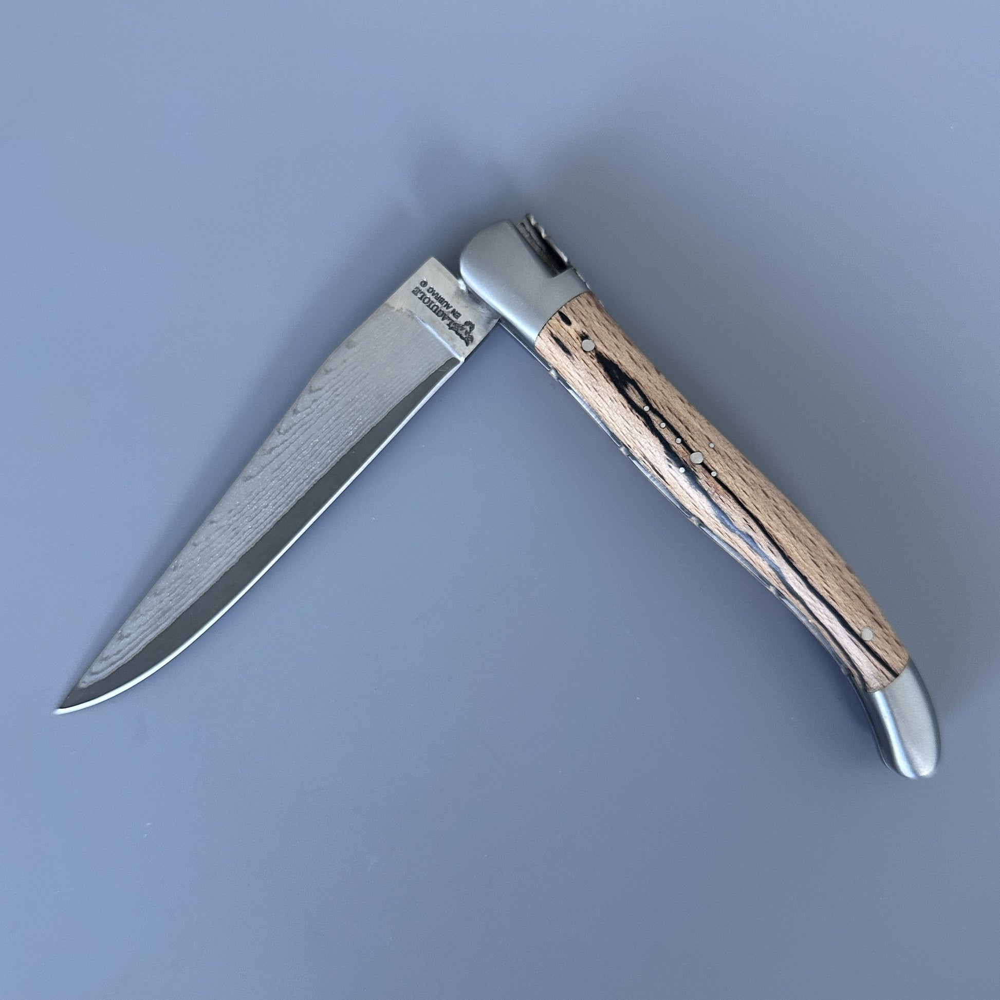 Reverse side of the Laguiole Double Plate Damascus knife, open, showing the Aubrac wood grain and Damascus blade.
