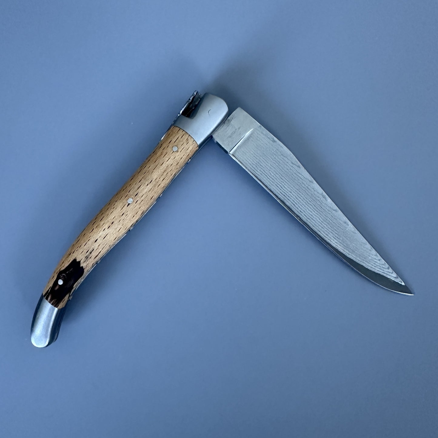 Reverse side of the Laguiole Double Plate Damascus knife, open, showing the Aubrac wood grain and Damascus blade with different wood pattern