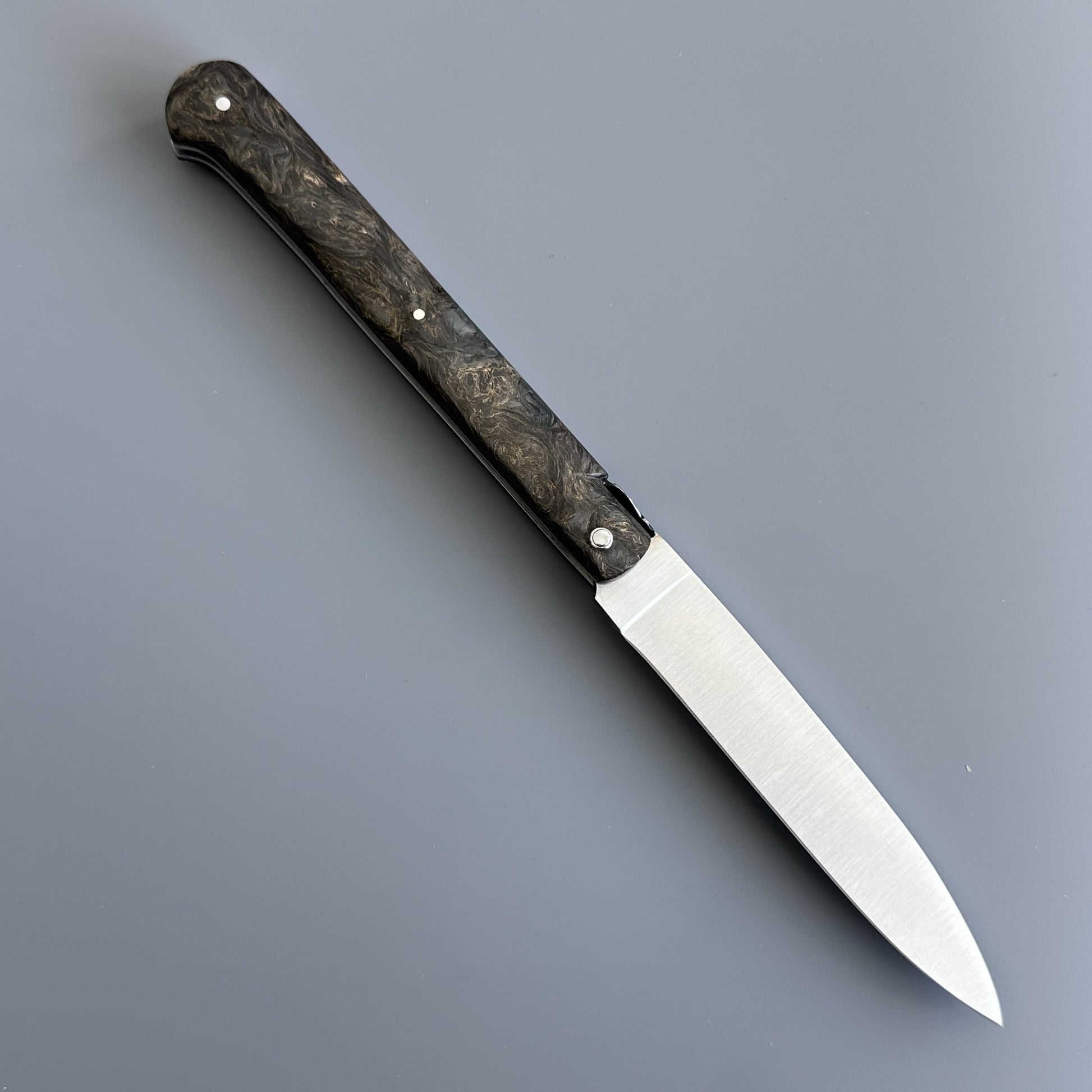 Laguiole Droit knife open on a gray background, showing the rounded Bourbonnaise blade profile and dark burl handle