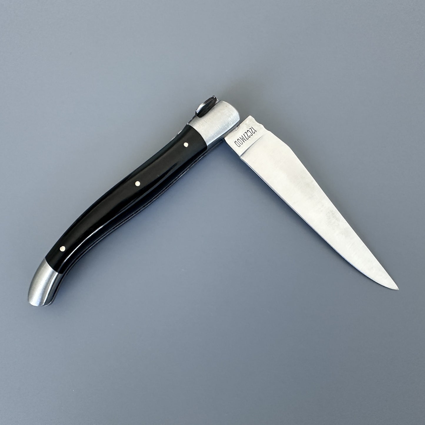 Laguiole en Aubrac folding knife with glossy black ebony handle, shown open on a gray background