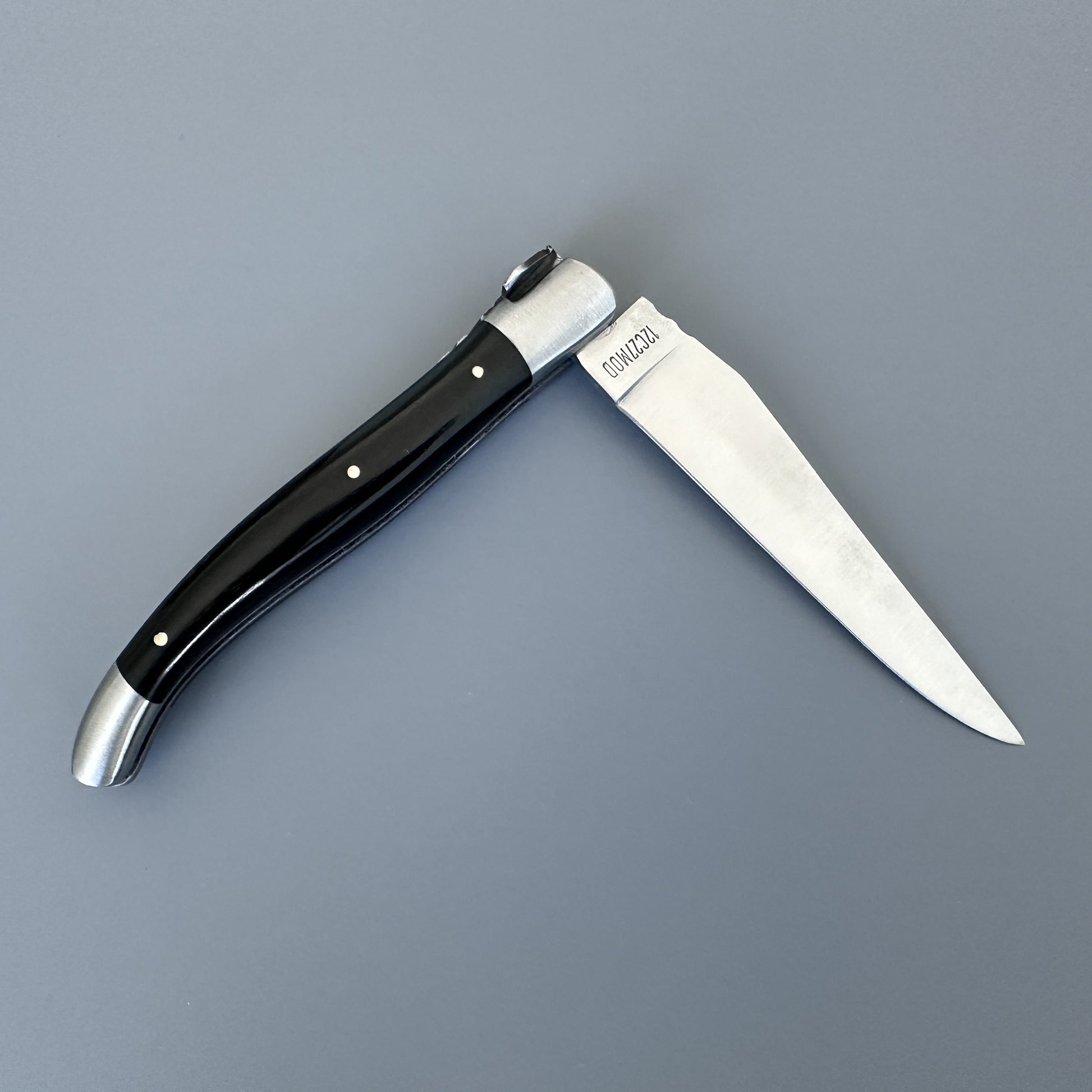 Laguiole en Aubrac folding knife with glossy black ebony handle, shown open on a gray background