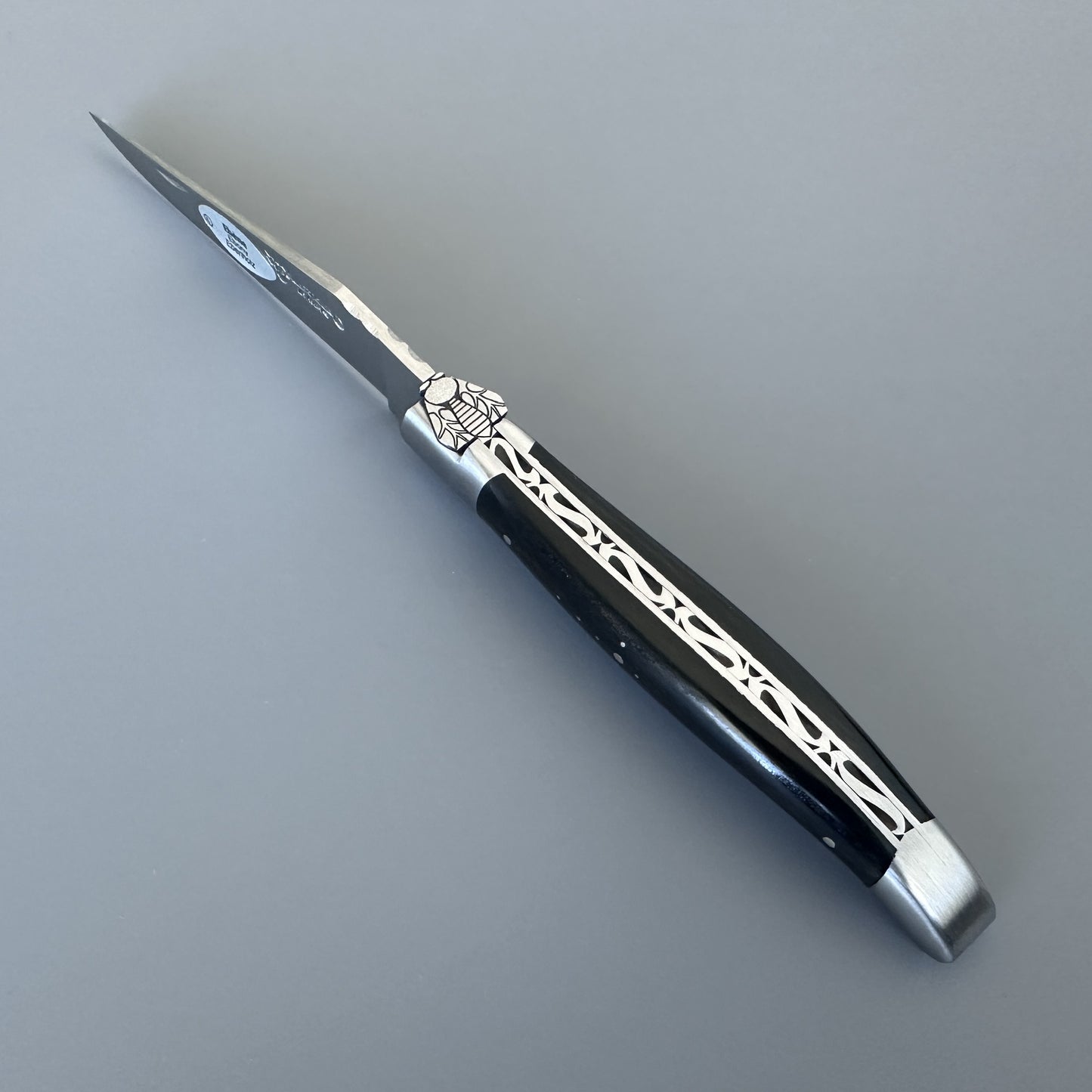 Laguiole en Aubrac knife open, angled to show the hand-engraved bee and silver filigree inlay along the ebony handle