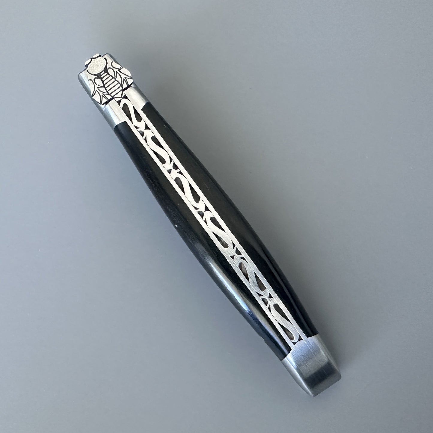 Close-up of the ebony handle's silver filigree inlay and hand-carved bee at the bolster of a Laguiole en Aubrac knife