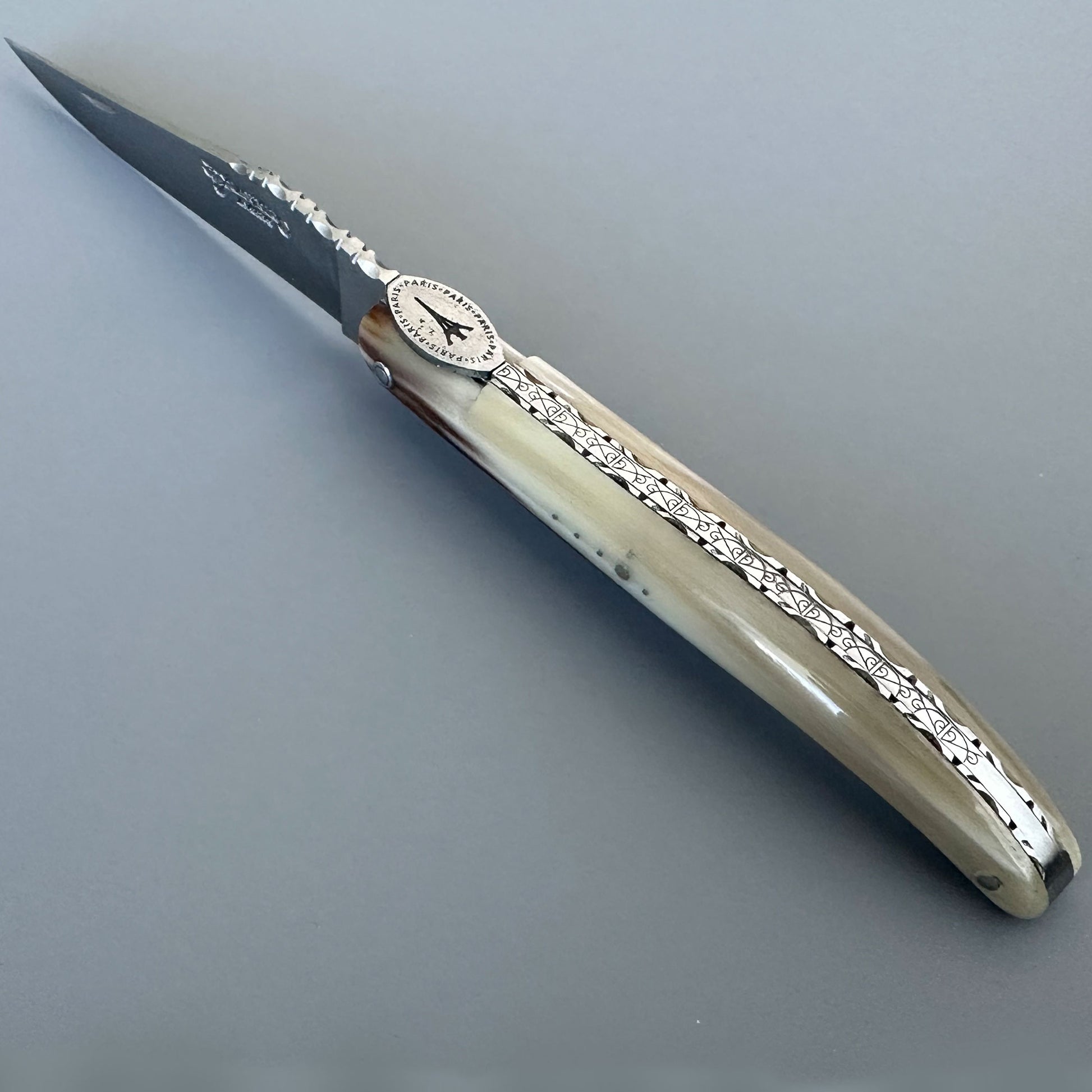 An ornate laguiole en Aubrac folding pocket knife with a silver-engraved handle and a dark steel blade, shown on a neutral gray background.