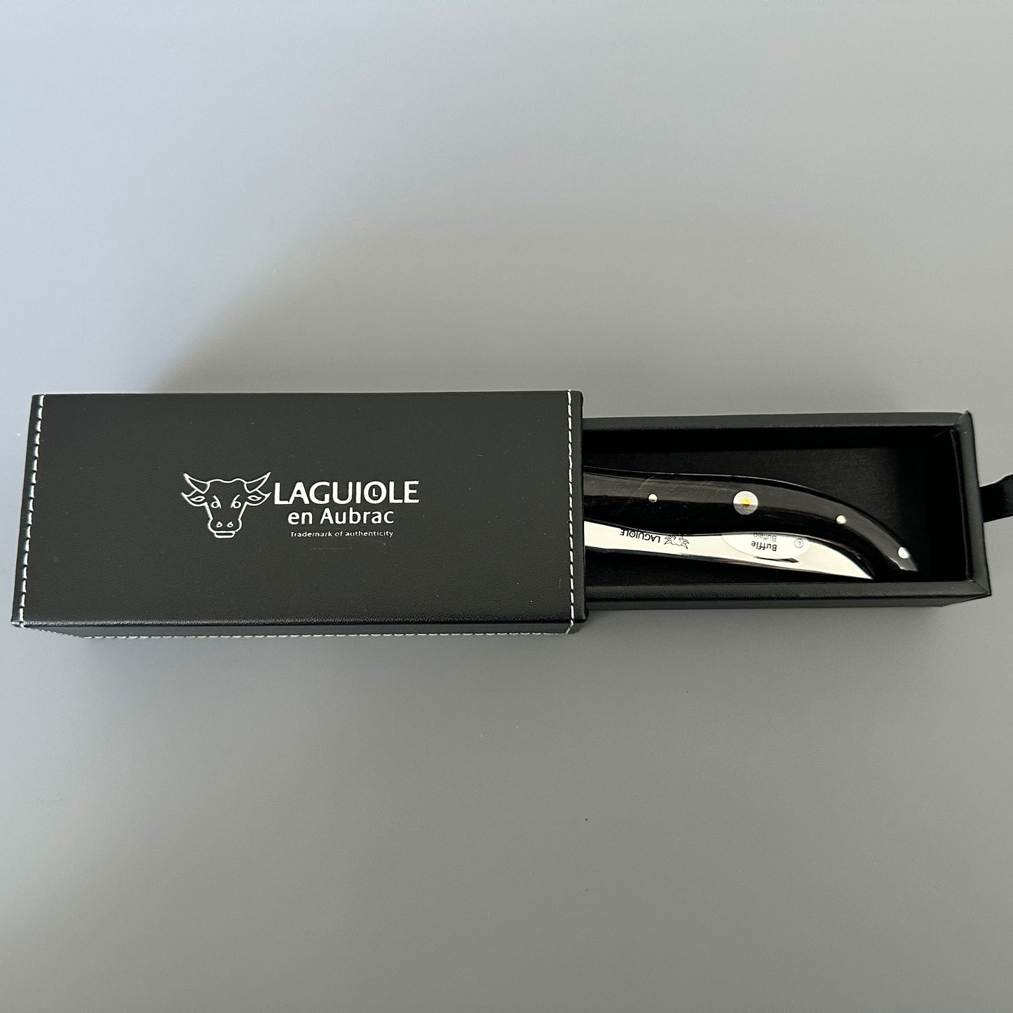Laguiole en Aubrac folding knife with its black buffalo-horn handle inside leather drawer case.