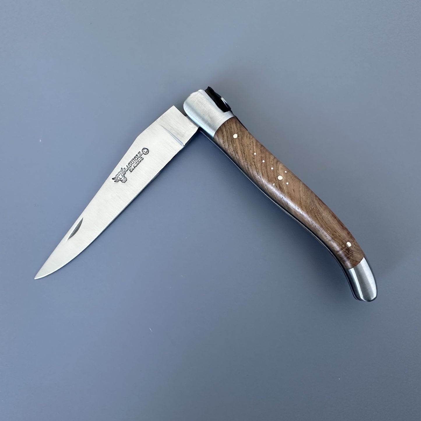 Laguiole en Aubrac folding knife with teak handle, shown open on a gray background, blade etched with the Laguiole bull logo