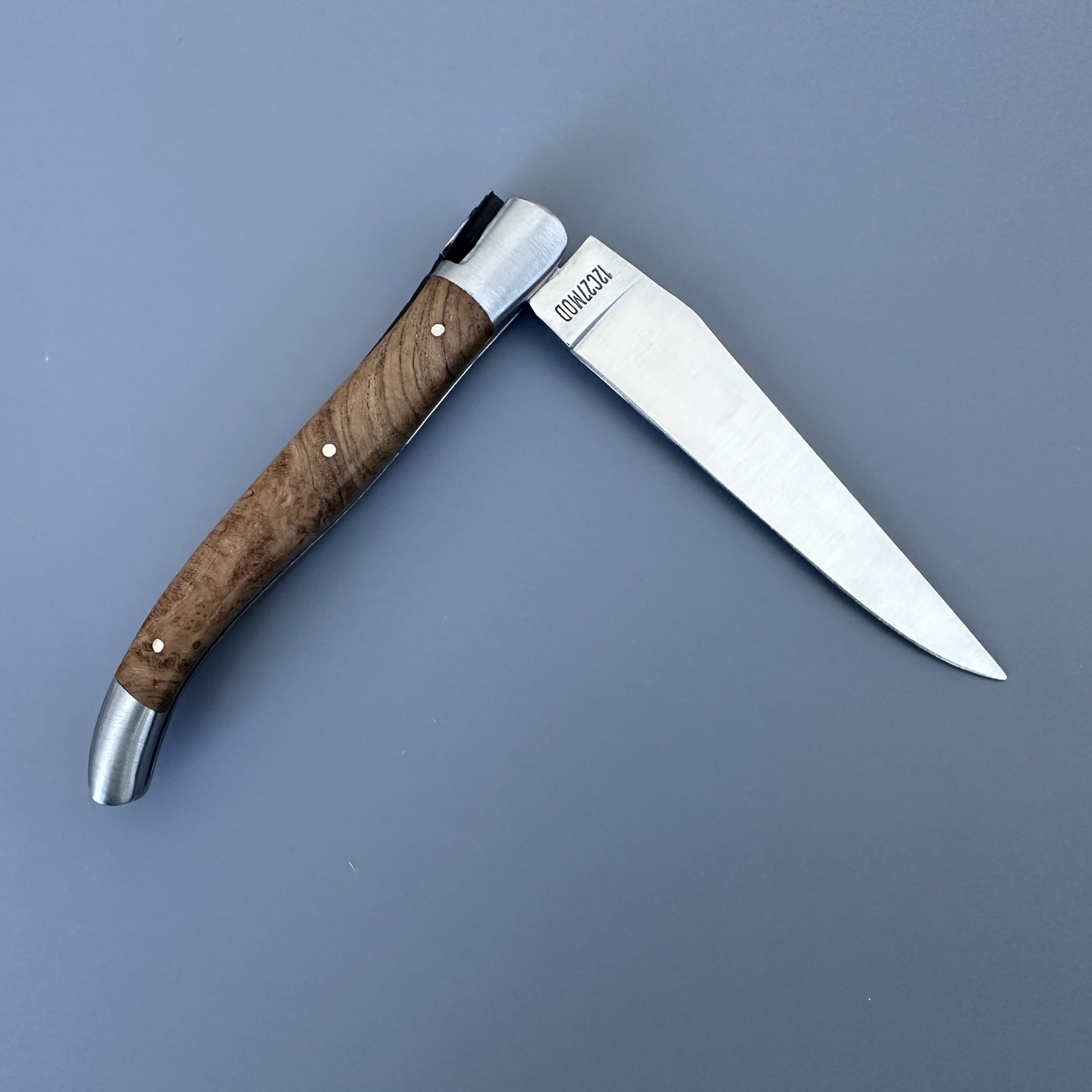 Laguiole en Aubrac knife open and reversed, showing the teak wood grain and blade etched with the Laguiole bull logo