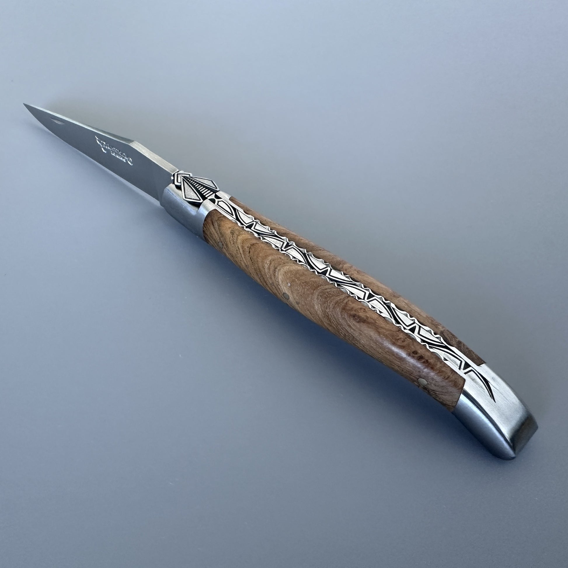 Laguiole en Aubrac knife open, angled to show the special hand-carved bee and geometric silver inlay along the teak handle