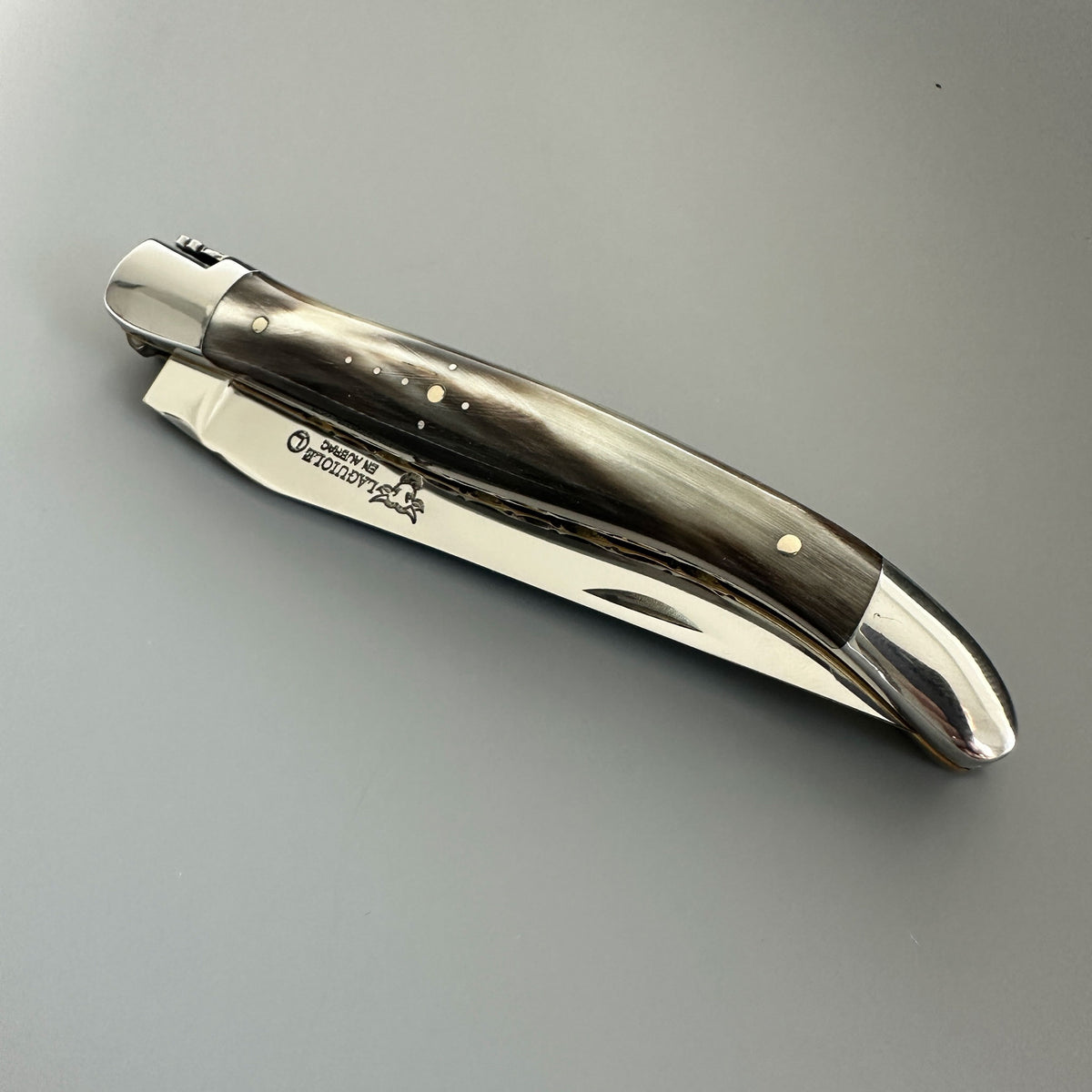 Laguiole en Aubrac double-plated pocket knife with a solid horn handle in closed position over a gray background