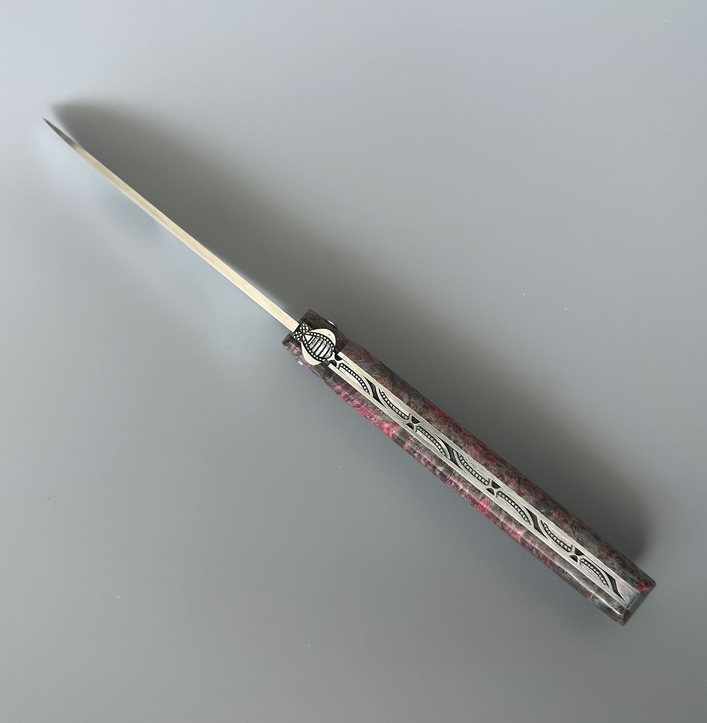 A folding pocket knife with a silver stainless steel blade and a textured handle featuring a pink and gray pattern with silver engraved details, shown on a neutral gray background.