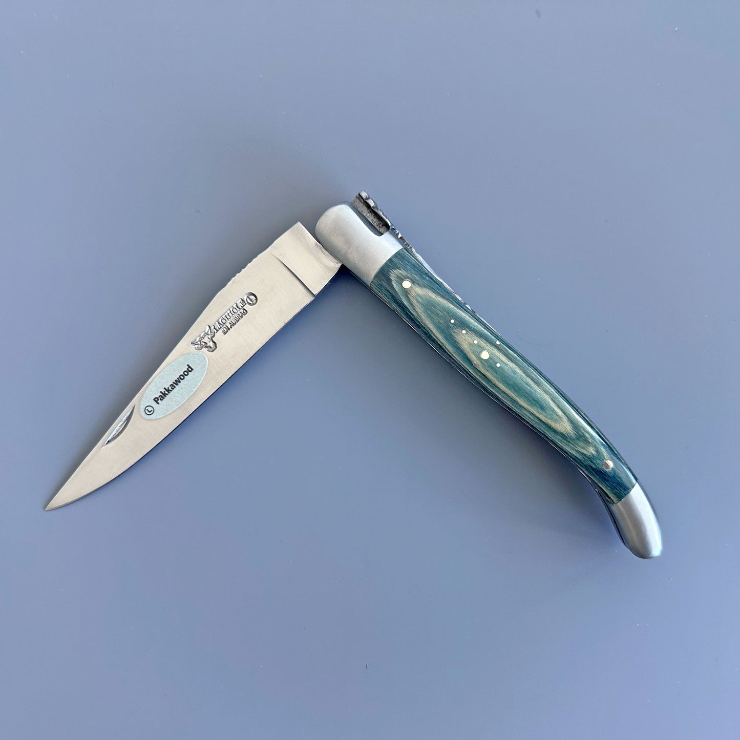 Laguiole en Aubrac folding knife with Blue  Pakka wood handle and forged bee spring, shown open on a gray background