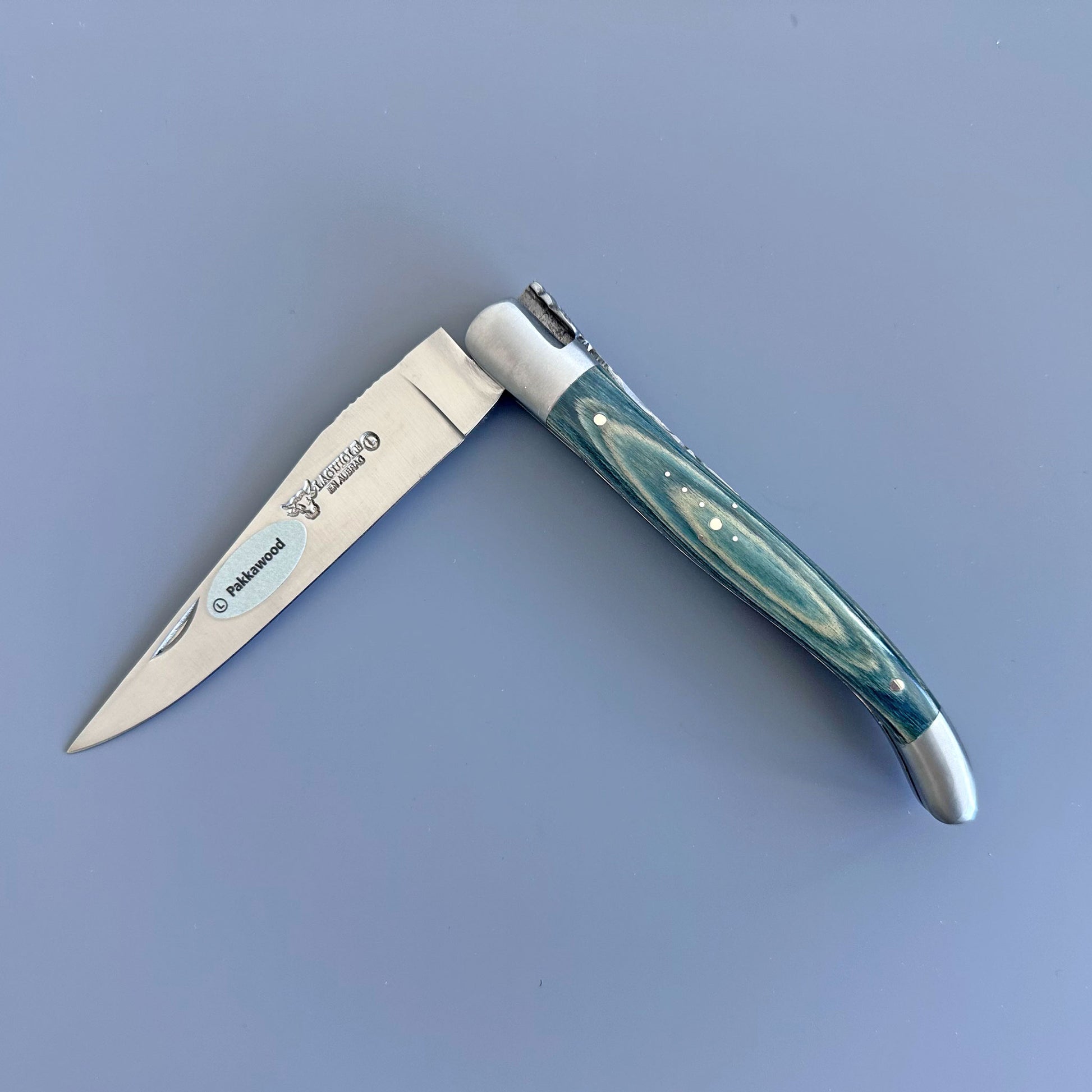 Laguiole en Aubrac folding knife with Blue  Pakka wood handle and forged bee spring, shown open on a gray background