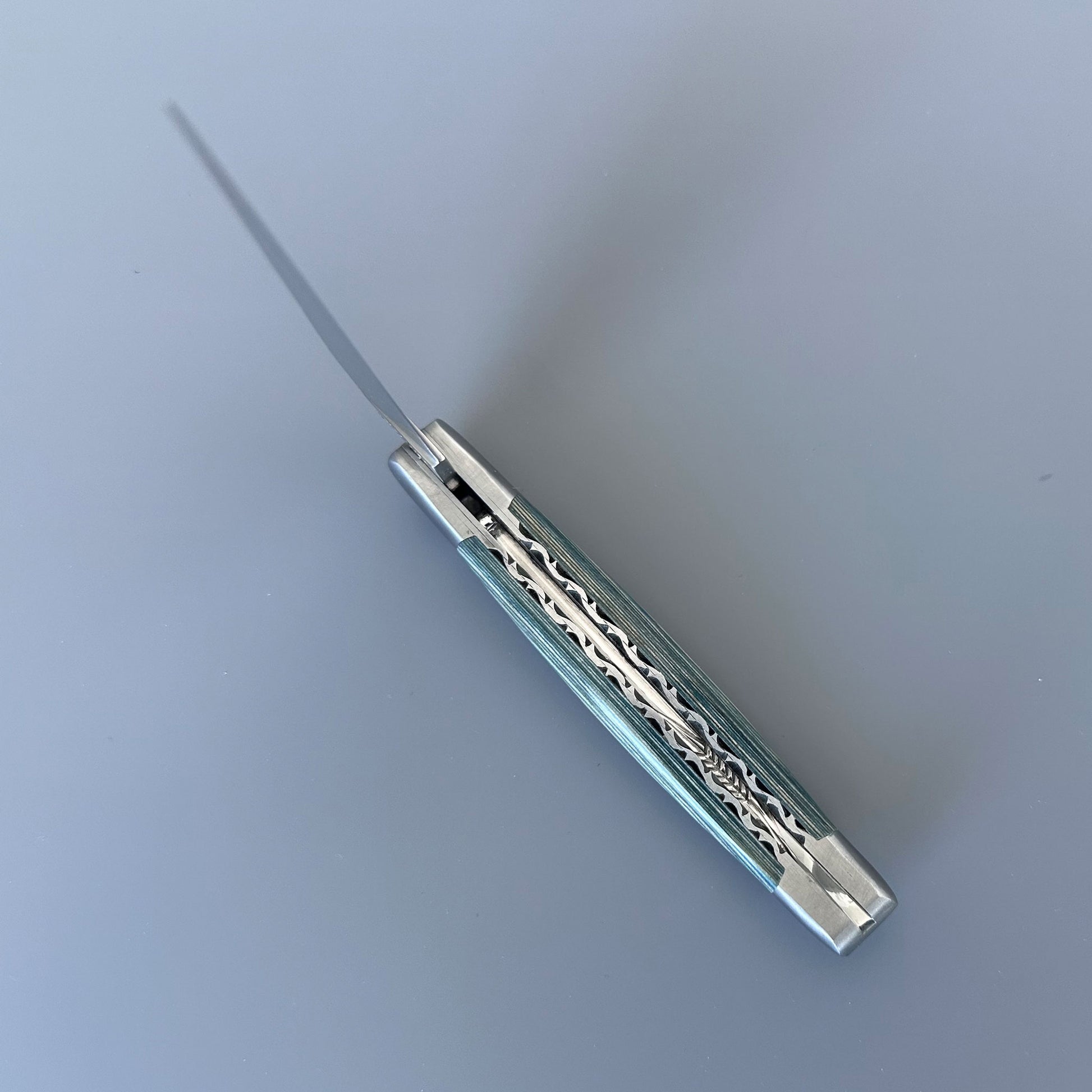 Close-up of the double-plated spine on a Laguiole en Aubrac knife, showing hand-carved blue Pakka handle scales