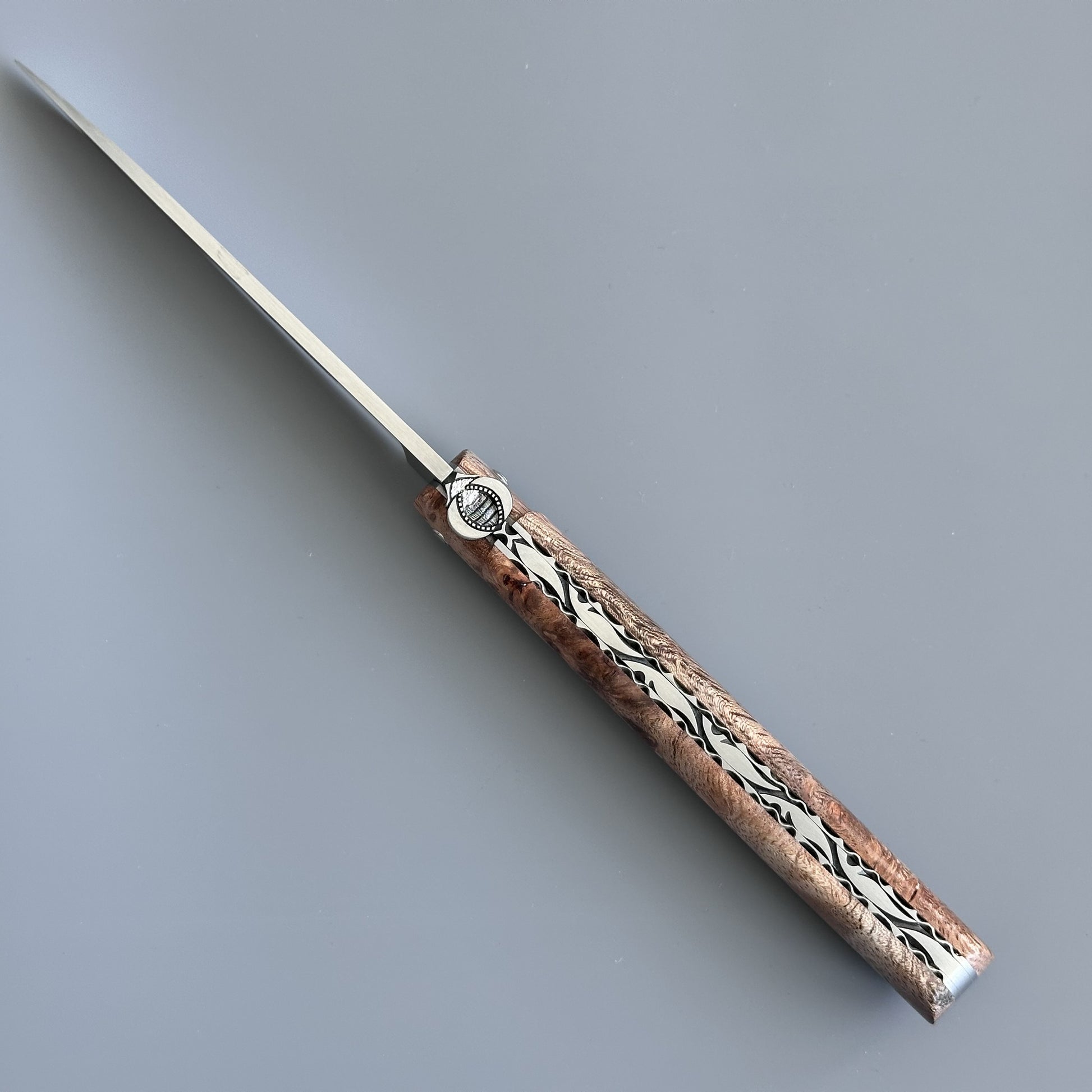 A Albizia wood handle folding knife from Laguiole en Aubrac showing detailed spine plate and bee.