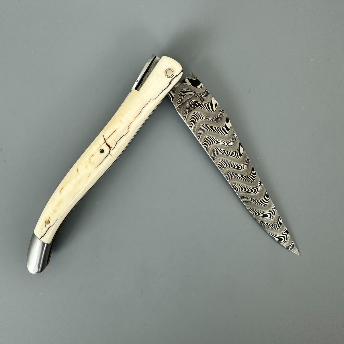 Reverse side of Laguiole en Aubrac folding pocket knife with a damascus blade and a mammoth ivory crust 