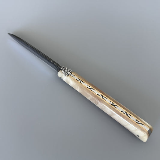 A pocket knife with a polished silver-colored metal blade and a handle made of cream-colored bone black inlay patterns, resting diagonally on a neutral gray background.
