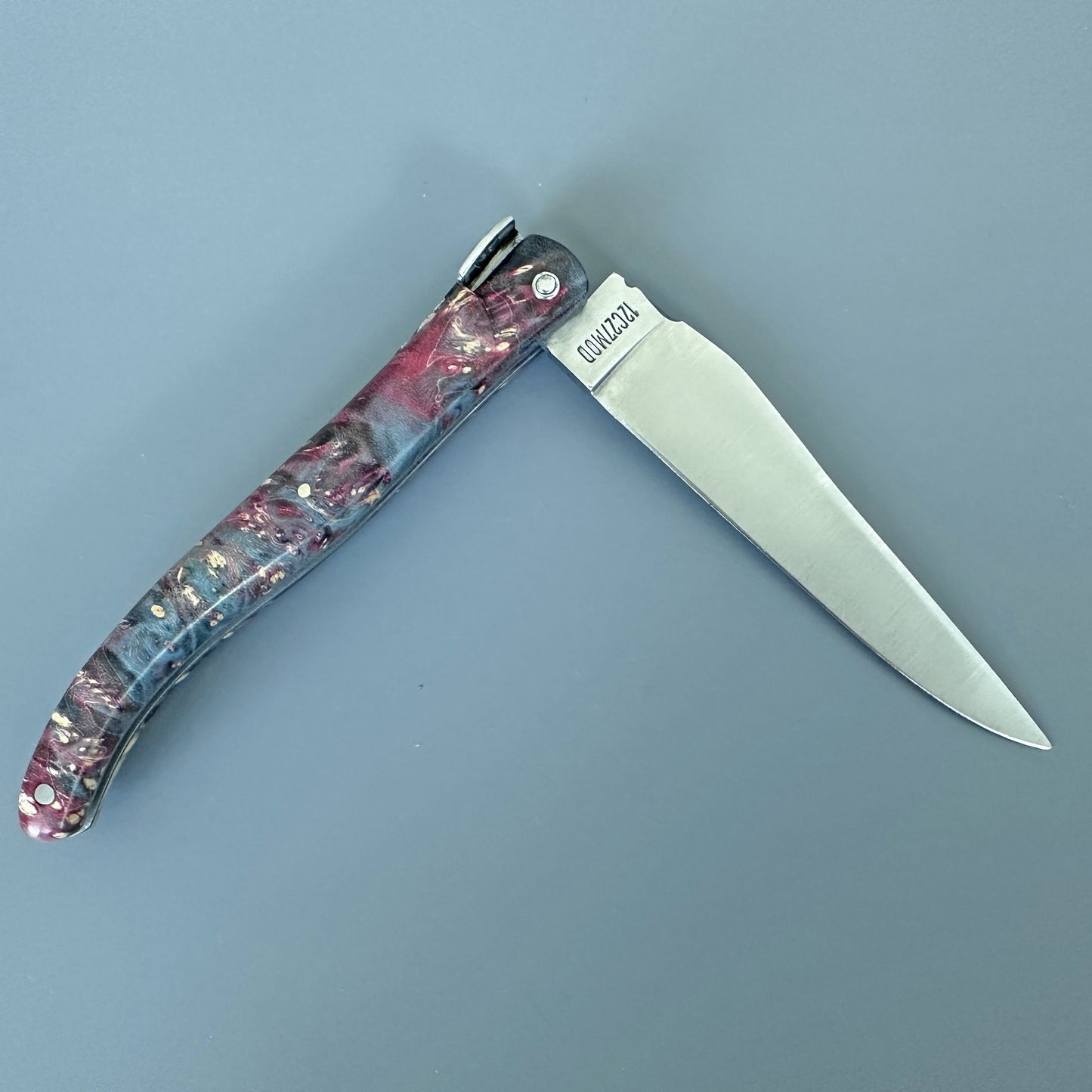 An open folding pocket knife with a textured, marbled handle in shades of pink gray, and cream, featuring a silver stainless steel blade. 