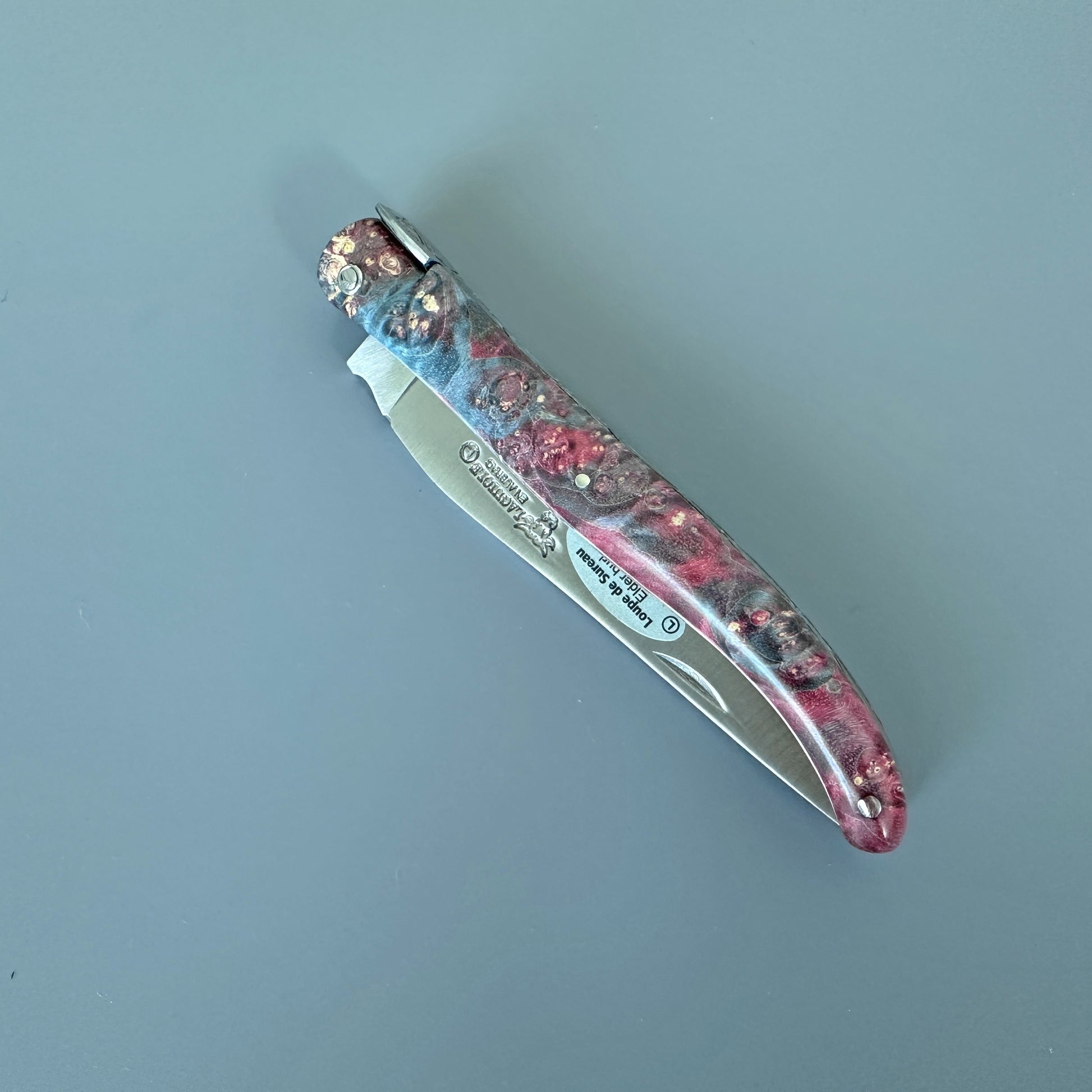 A folding pocket knife  in closed position with a marbled resin handle in blue, red,  featuring a silver stainless steel blade. 