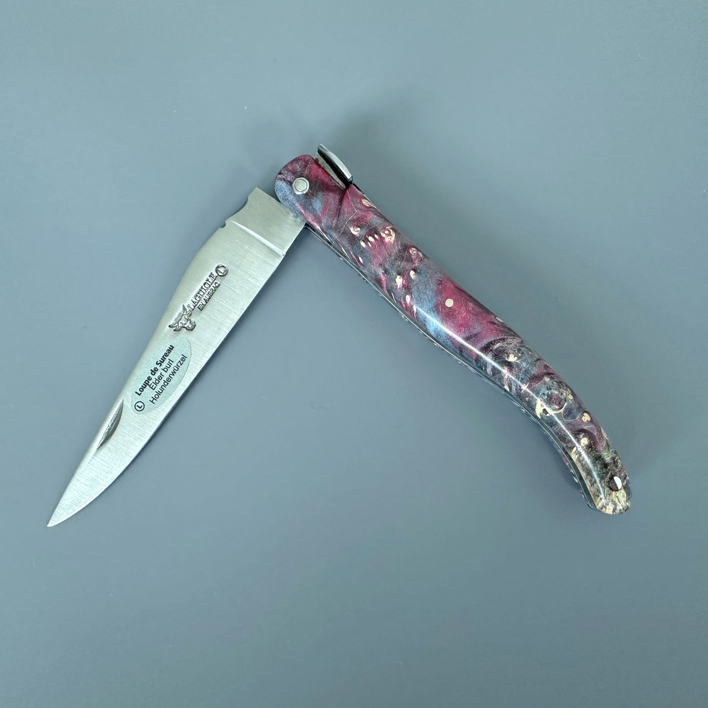 An open folding pocket knife with a silver stainless steel blade and a marbled resin handle in pink, purple, blue shown on a solid gray background.