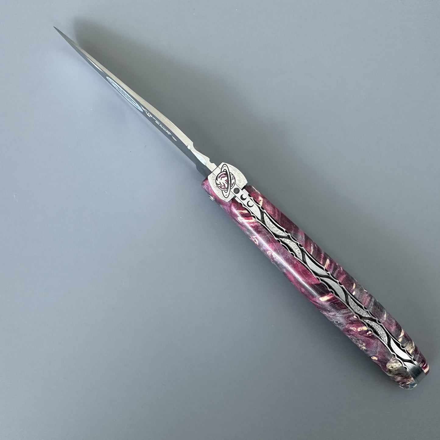 A folding pocket knife with a satin silver blade and a pink marbled handle featuring silver wave-like inlay details, shown on a neutral gray background.