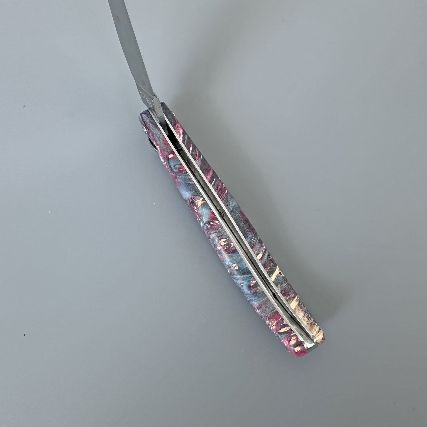 A folding pocket knife with a marbled resin handle in pink, blue, and cream, shown partially open on a neutral gray background.