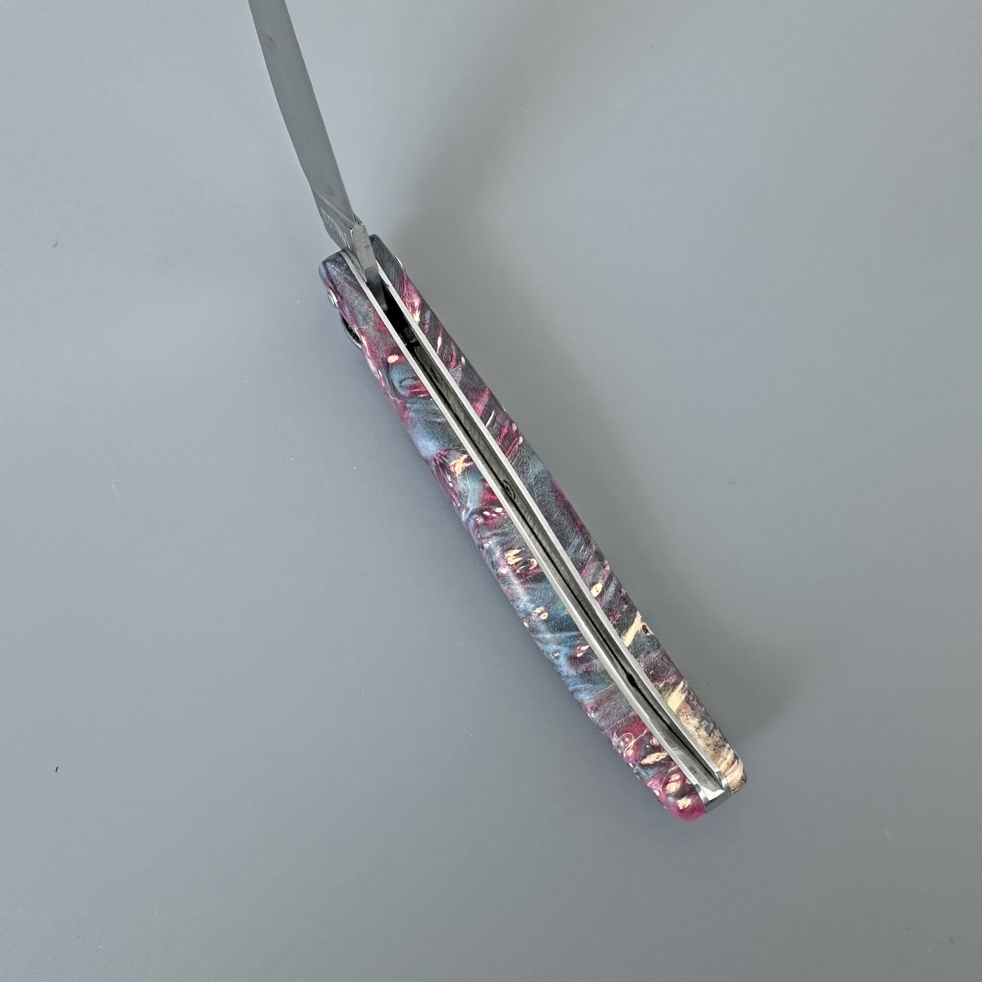 A folding pocket knife with a marbled resin handle in pink, blue, and cream, shown partially open on a neutral gray background.